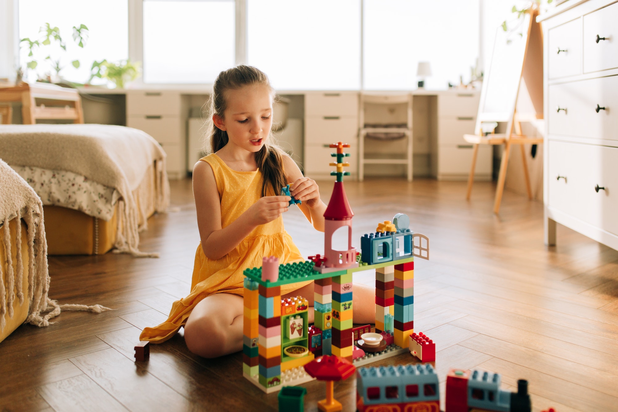 Little toddler girl playing with Lego blocks at home alone